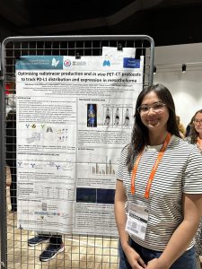 Dr Tracy Hoang stands in front of a scientific poster with the title 'Optimising radiotracer production and in vivo PET-CT protocols to track PD-L1 distribution and expression in mesothelioma.